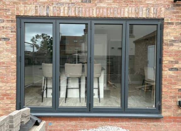 An outside view of a kitchen with a set of grey composite bi-fold doors.